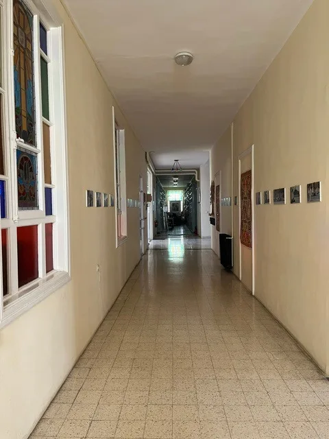Un corridoio con vetrate colorate su un lato e una fila di piccole fotografie incorniciate sull’altro