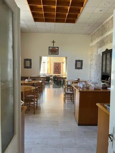 La sala da pranzo vista da una porta: tavoli rotondi, un bancone con tazze e ciotole e una parete in pietra